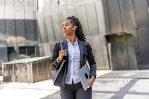 Portrait of a latin businesswoman walking distracted carrying laptop in the city next to a modern building