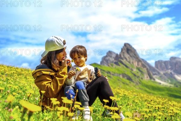 Tourists enjoying summer in the italian alps, smelling wildflowers with the odle mountains in the background