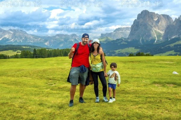 Family enjoying summer vacation hiking in alpe di siusi, with the sciliar mountain in the background