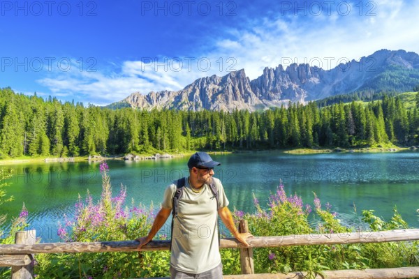 Hiker admiring the stunning turquoise waters of lake carezza with the latemar mountain range in the background, located in the italian dolomites