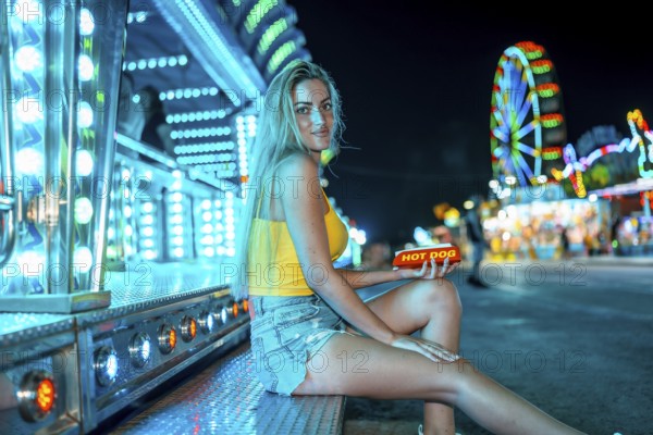 Side view photo of a woman in a night fair about to eat a hot dog