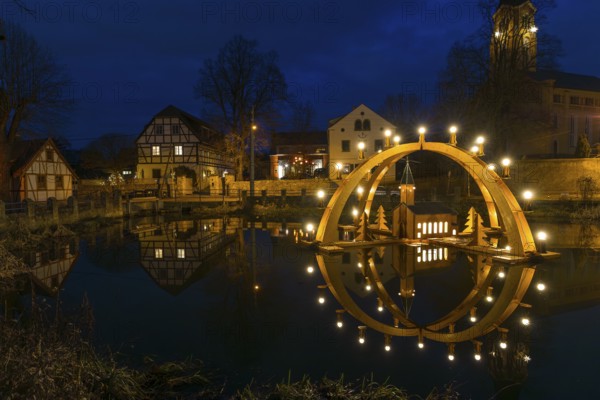 Floating double candle arch from the Ore Mountains with model of the church on the village pond, behind it the village church of Bärnsdorf, Radeburg, Saxony, Germany, Europe
