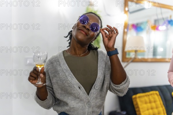 Cool african woman in sunglasses drinking wine in the living room during a home party