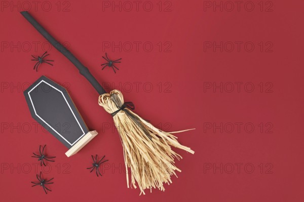 Halloween witch broom, coffin shaped chalkboard and spiders on dark red background with copy space
