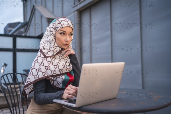 Arab girl with a white veil at the computer on the terrace of a coffe shop, contrabass with the computer. Modern Arab young man with new technologies
