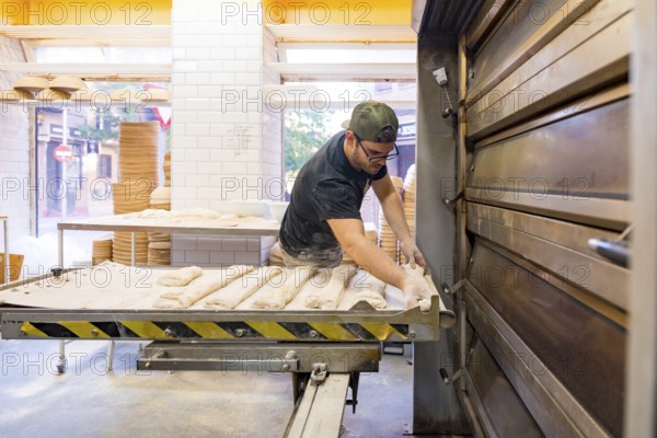 The employee placing the bread before the oven in an artisan bakery workshop