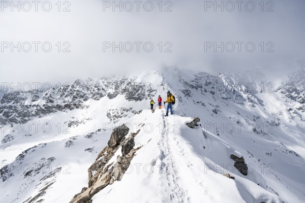 Three mountaineers climbing the narrow ridge of Piz Laviner, view of mountain panorama in winter mountain landscape, Grisons Haute Route, Albula Alps, Rhaetian Alps, Grisons, Eastern Switzerland, Switzerland, Europe