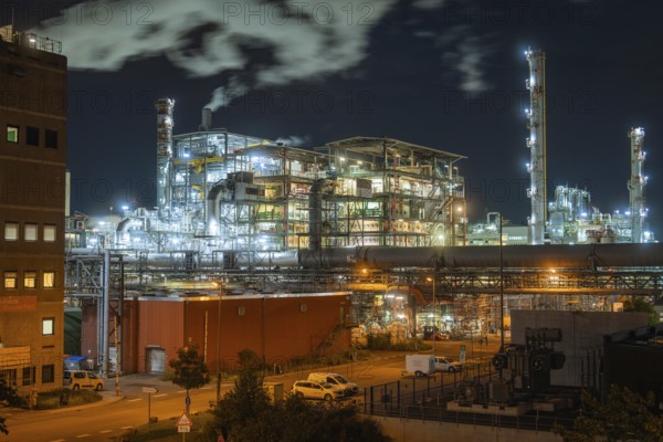 Illuminated industrial plant at night with smoking chimneys and vehicles on the road in the foreground, Mannheim, Germany, Europe