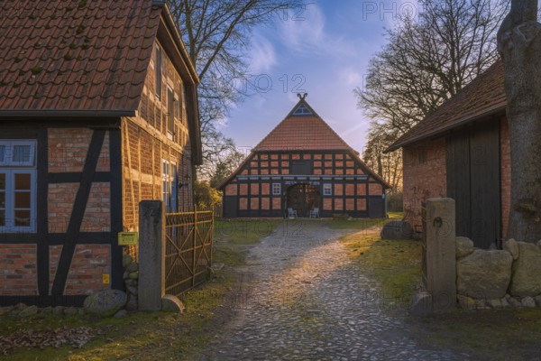 View of a courtyard entrance with a half-timbered farmhouse behind it in the evening light, Otersen, Kirchlinteln, Verden, Aller Leine Valley, Lower Saxony, Germany, Europe
