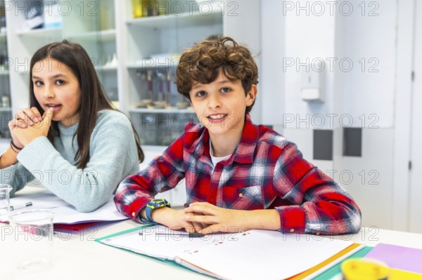 Smiling students sitting at desk in science classroom, learning and interacting during lesson, notebooks and educational materials visible