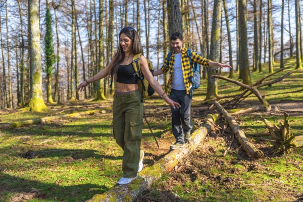 Hikers with backpacks carefully balancing on fallen tree trunk while enjoying hike through sunny forest