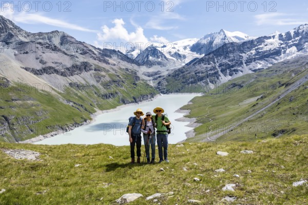 Three friends, mountaineers in front of a blue mountain lake, reservoir Lac des Dix, behind mountain peak Mont Blanc de Cheilon with glacier, Hérménence, Valais Alps, Valais, Switzerland, Europe