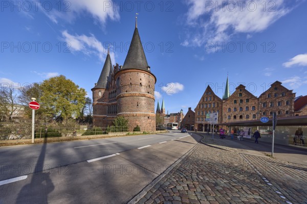 Lübeck Holstentor, side view, pedestrian crossing, cobblestone pavement, blue sky with fair weather clouds, intersection Wallstraße with Holstentorplatz, Hanseatic city of Lübeck, Schleswig-Holstein, Germany, Europe