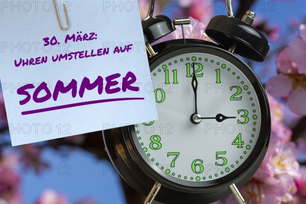 (Photomontage) Summer time changeover Symbolic image: Alarm clock before almond blossom and text 30 MARCH: CLOCK CHANGEOVER TO SUMMER