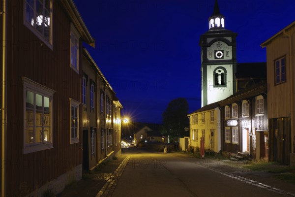 City street at night with illuminated buildings and an illuminated church in the background, Unesco World Heritage Site, miners' town, Röros, Norway, Europe
