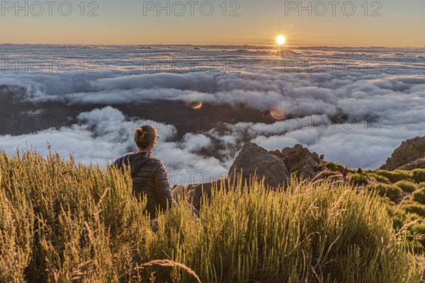 A hiker watches the sunset over a sea of clouds from a mountain top, Pico Ruivo, Madeira, Portugal, Europe