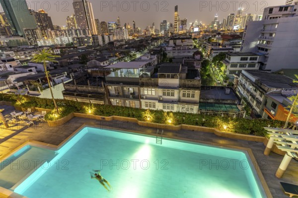 Illuminated swimming pool in front of the city view and skyline of Bangkok at dusk, Thailand, Asia