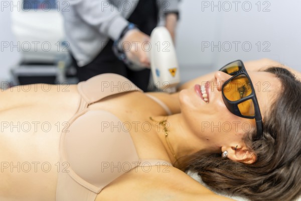 Beautiful and attractive adult woman receiving depilatory treatment on armpit lying on the clinic