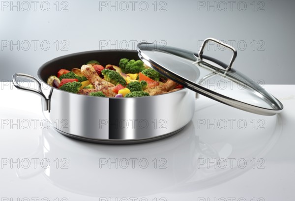 Cooking pot with vegetables and chicken thighs in front of a white background, studio shot