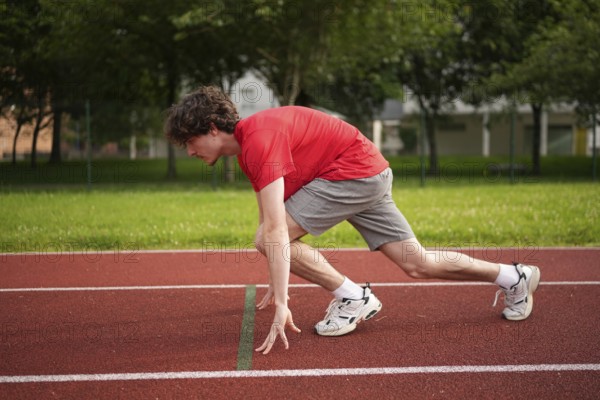 Side view full length of a caucasian young male runner in the starting line of a track ready to start running