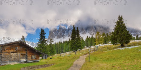 Panoramic view of the partly cloudy Geißler group with a hiking trail and a hut of the Glatsch Alm in the foreground