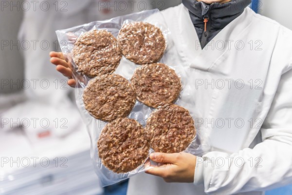 Unrecognizable female worker holding a package of fresh vacuum sealed hamburgers in a factory