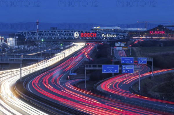 A8 motorway at Stuttgart Airport in the evening. Heavy traffic, lanes of light. Modern architecture of Messe Stuttgart with multi-storey car park above the motorway lanes. Logo of the Bosch company. Stuttgart, Baden-Württemberg, Germany, Europe