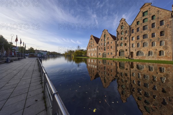Historic salt warehouses, brick buildings reflected in the morning light on the water surface of the Trave, quay wall with railings, Hanseatic city of Lübeck, independent city, Schleswig-Holstein, Germany, Europe