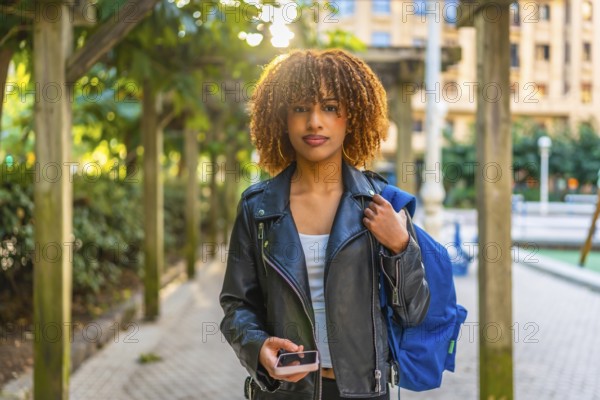 Frontal portrait of a beauty and confident latin woman using smartphone walking down the street