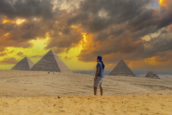A young man in a blue turban walking next to the Pyramids of Giza, the oldest Funerary monument in the world. In the city of Cairo, Egypt, Africa