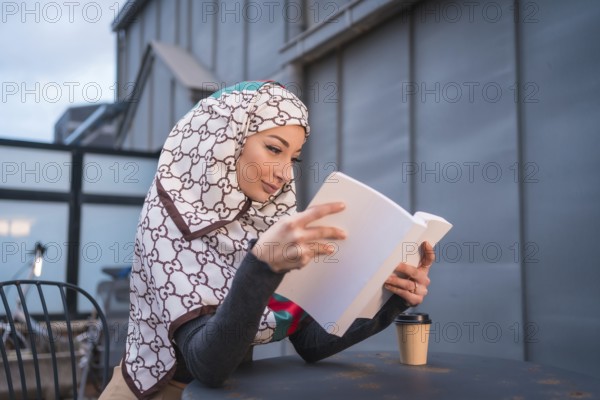 Arab girl with white veil at the computer on the terrace of a coffe shop, having a lot of fun reading a beautiful book