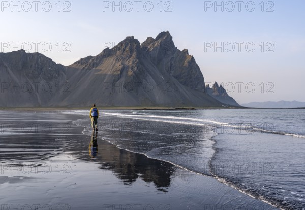 Tourist at black lava beach, sandy beach and sea, mountains Klifatindur reflected in the water, Eystrahorn and Kambhorn, headland Stokksnes, mountain range Klifatindur, Austurland, East Iceland, Iceland, Europe
