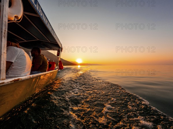 View from below along the orange sunset water of Shkoder Lake in Shiroka from a tourist boat. Albania
