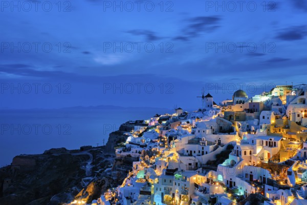 Famous greek iconic picturesque tourist destination Oia village with traditional white houses and windmills in Santorini island in the evening blue hour, Greece, Europe