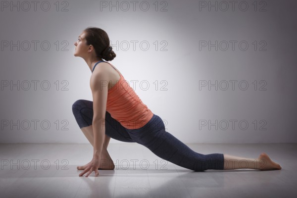 Beautiful sporty fit yogini woman practices yoga asana Anjaneyasana, low crescent lunge pose in surya namaskar in studio