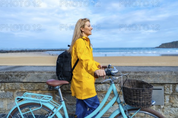 Tourist walking with her bicycle along the beach promenade on a cloudy day, enjoying the seascape