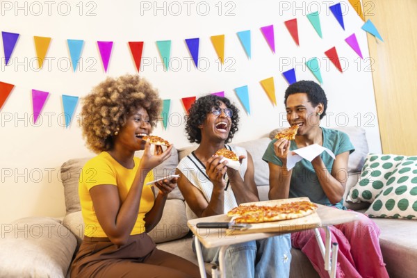 Diverse friends eating a slice of pizza sitting on the sofa celebrating at home