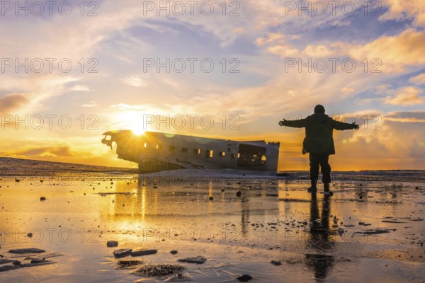 Young adventurous man at sunrise on Solheimasandur plane in winter in Iceland, with open arms