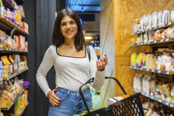 Young woman smiling and choosing organic products in a supermarket, holding a shopping basket