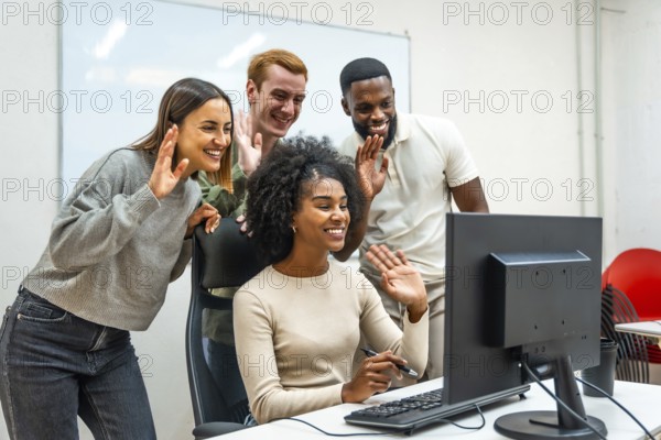 Team of diverse coworkers waving at screen during online meeting together in the office