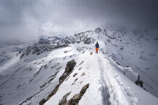 Mountaineer descending the narrow ridge of Piz Laviner, view of mountain panorama in wintry mountain landscape with dramatic clouds, Grisons Haute Route, Albula Alps, Rhaetian Alps, Grisons, Eastern Switzerland, Switzerland, Europe
