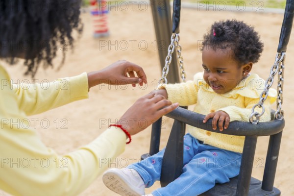 Close-up of a happy little african girl swinging with her mother in a park