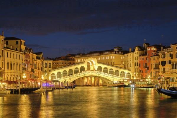 Famous Venetian tourist landmark Rialto bridge (Ponte di Rialto) over Grand Canal with vaporetto waterbus illuminated at night in Venice, Italy, Europe