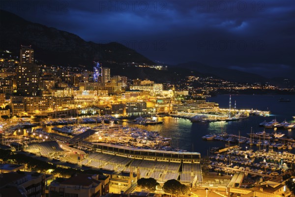 Aerial view of Monaco Monte Carlo harbour and illuminated city skyline in the evening blue hour twilight. Monaco Port night view with luxurious yachts