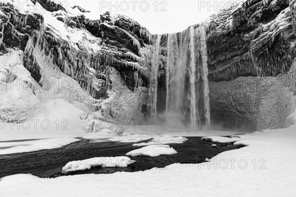 Skogafoss waterfall with icy and snowy rock face, black and white photo, Sudurland, Iceland, Europe
