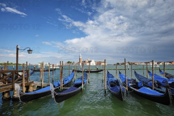 VENICE, ITALY, JUNE 27, 2018: Gondolas and gondolier in lagoon of Venice by Saint Mark (San Marco) square with San Giorgio di Maggiore church in background in Venice, Italy, Europe