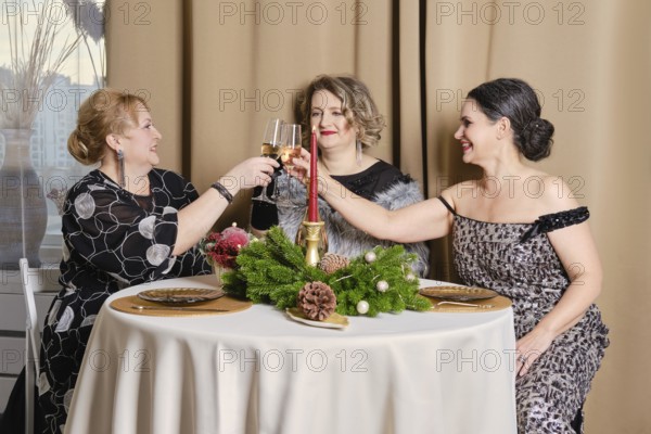Three juyful middle age women celebrating christmas sitting behind the festive table