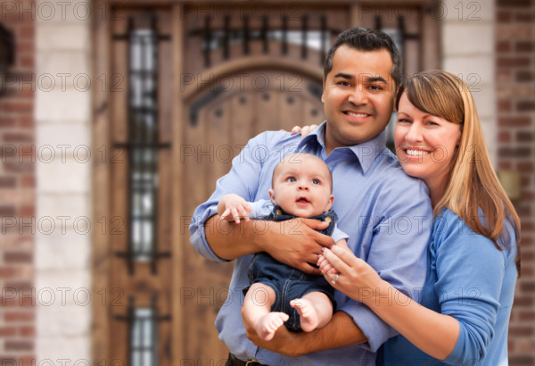 Happy mixed-race couple with baby in front of house