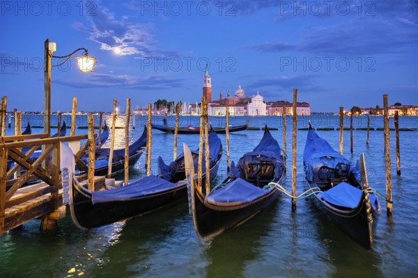 Romantic vacation Venice travel background, gondolas at Saint Mark (San Marco) square and Basilica San Giorgio Maggiore Church seen across Venice lagoon with full moon. Venice, Italy, Europe