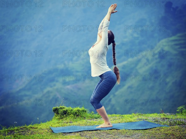 Young sporty fit woman doing yoga asana Utkatasana (chair pose) outdoors in mountains Himalayas in India. Vintage retro effect filtered hipster style image